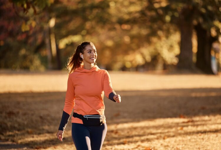 Happy sportswoman enjoying while walking in nature during autumn day.