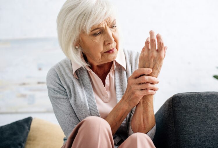 senior woman having hand Arthritis and sitting on sofa in apartment